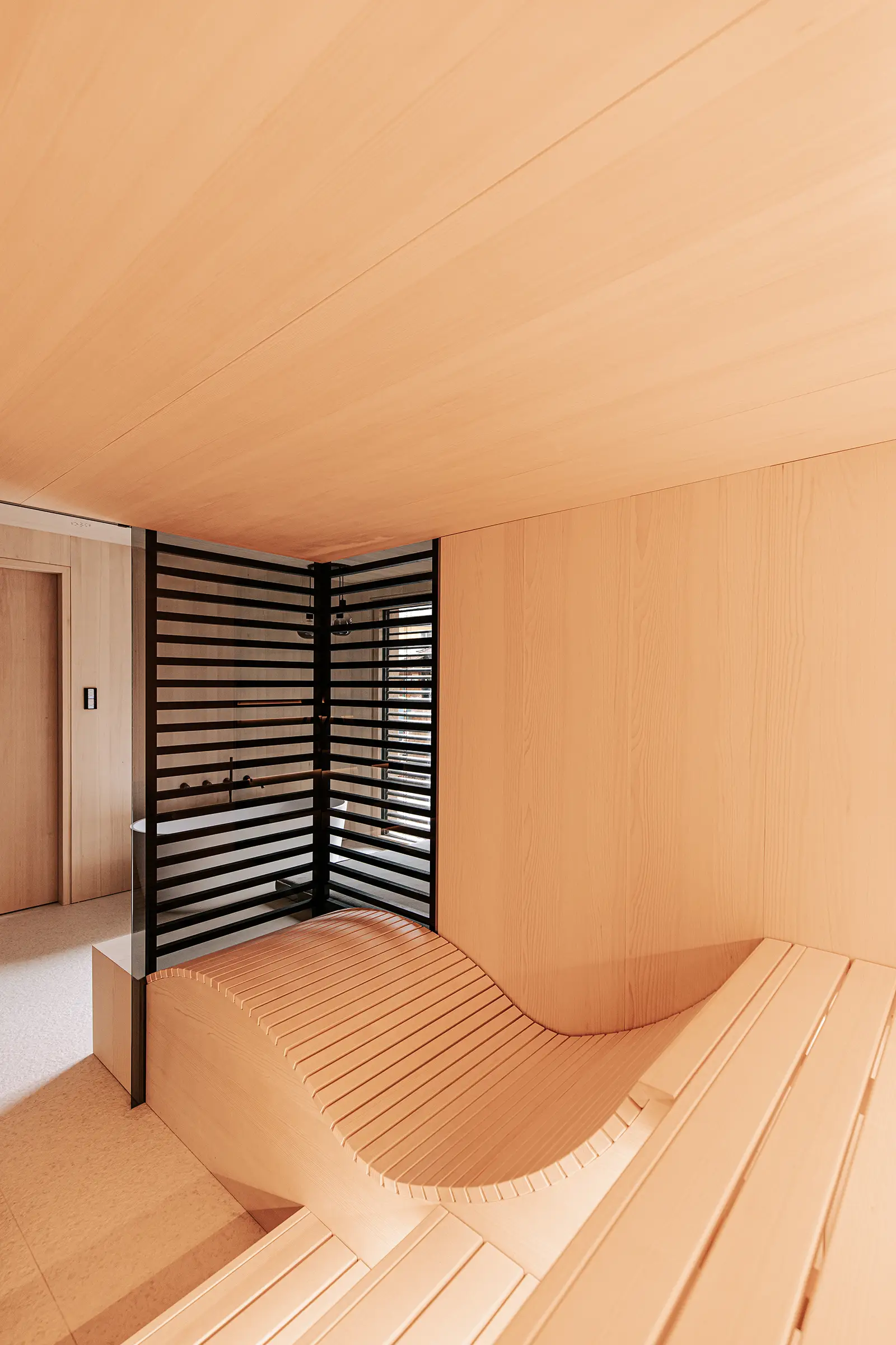 Minimalistische Sauna aus hellem Tannenholz mit ergonomischer Saunalieger und schwarzen Holzstreben als Sichtschutz