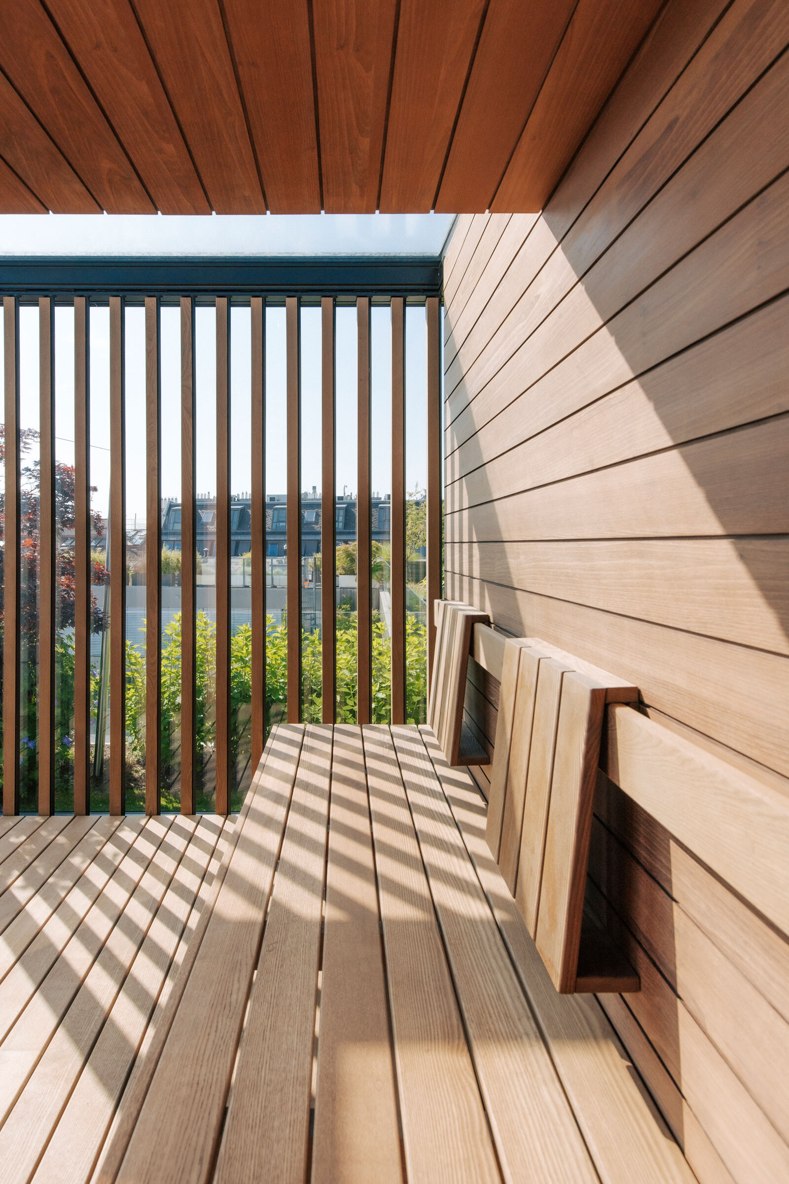 Minimalistische Sauna aus Akazienholz mit Sichtschutz aus Holzlamellen und Blick in einen Dachgarten