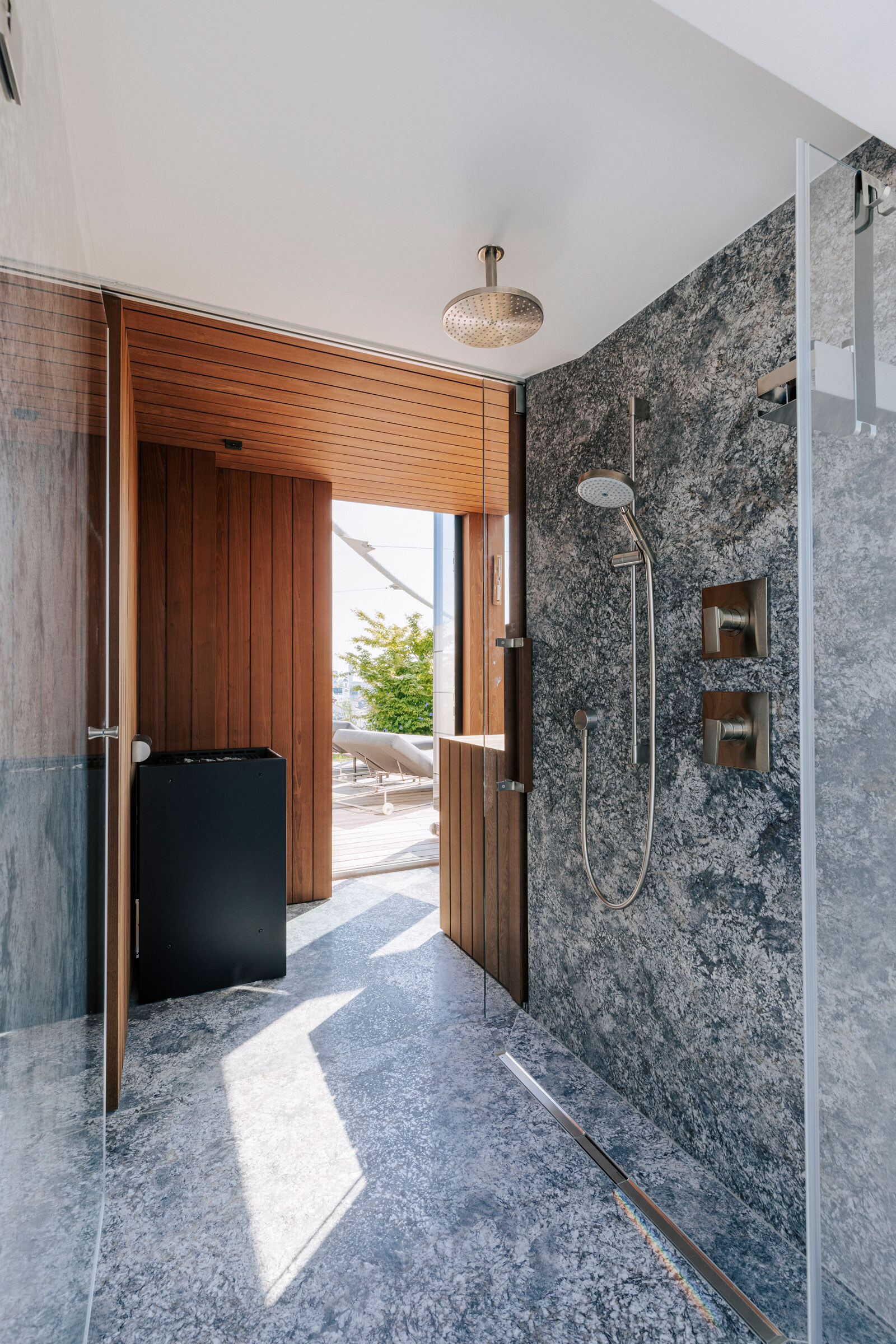 Bodenebene Dusche aus Naturstein mit anschließender Sauna aus dunklem Holz und Blick auf eine Terrasse