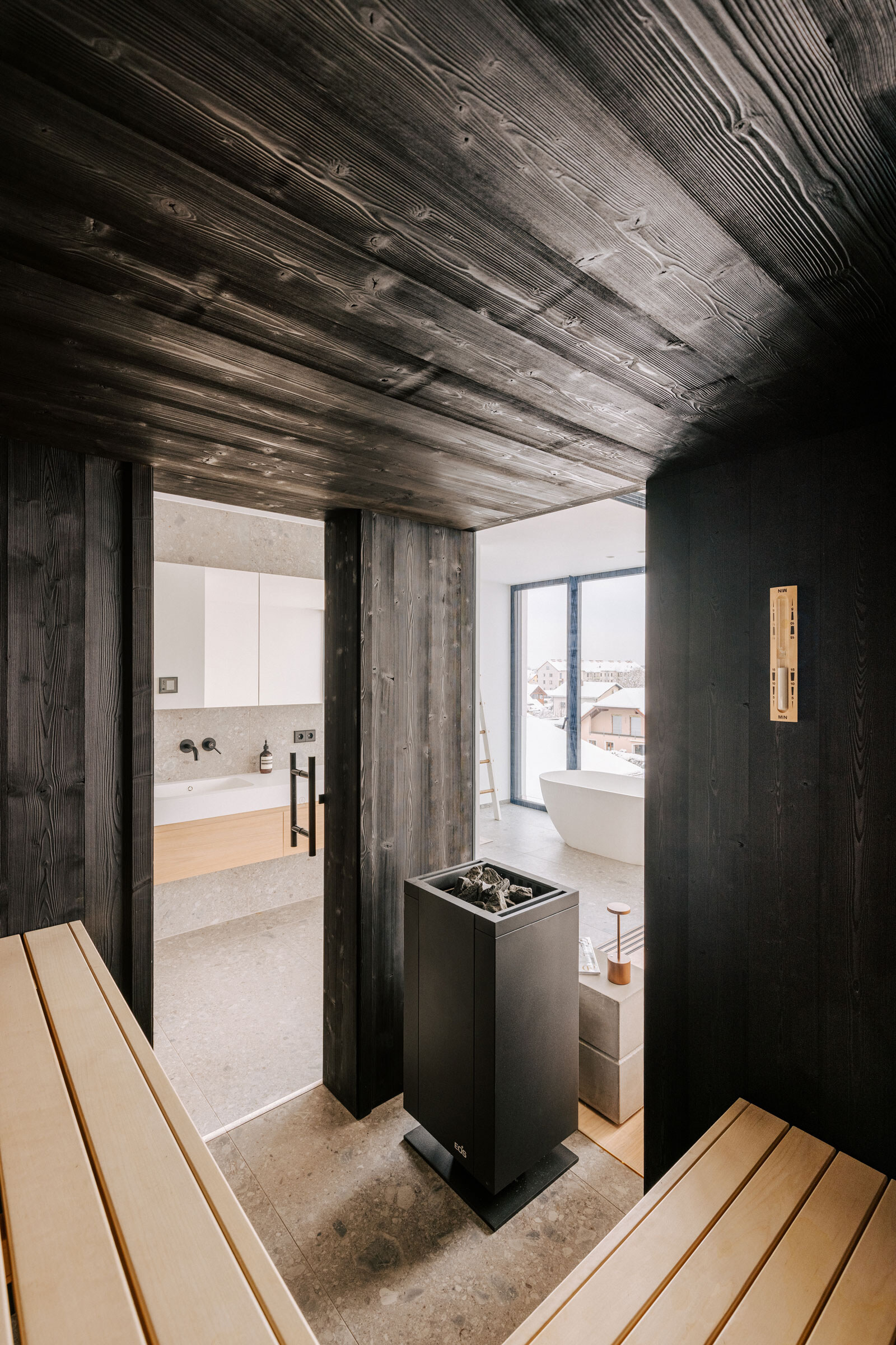 apandi-Sauna aus schwarzem Holz mit Glasfenstern und Ausblick in ein modernes Badezimmer mit freistehender Badewanne