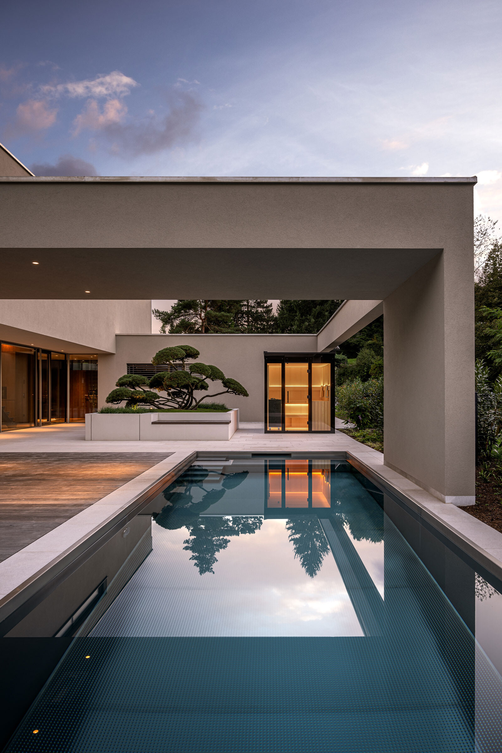 Minimalistische Außensauna aus Glas in modernem Design auf einer Terrasse mit Pool und Gartenbonsai