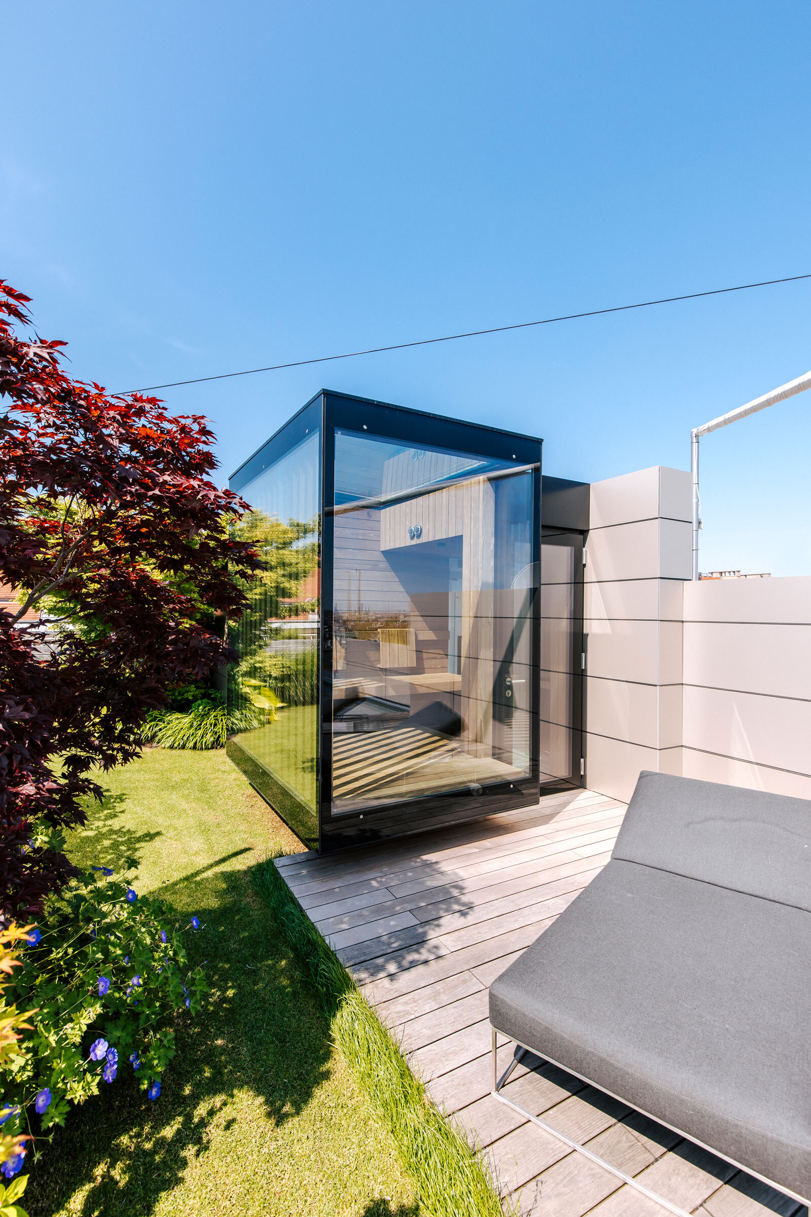 Moderne, verglaste Außensauna in minimalistischem Design auf einer begrünten Dachterrasse