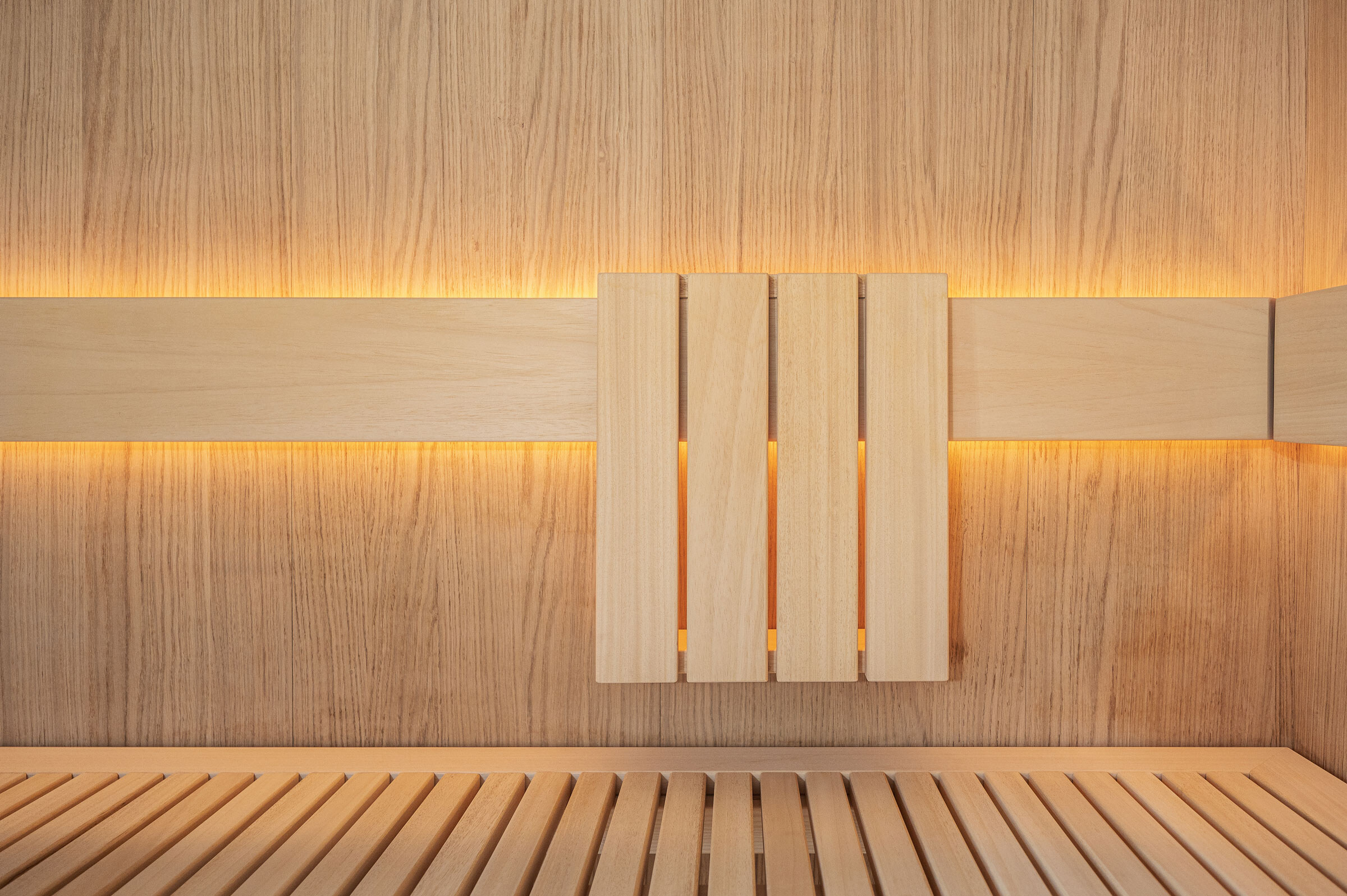 Rückenlehne aus hellem Holz einer sanft beleuchteten Sauna in minimalistischem Design