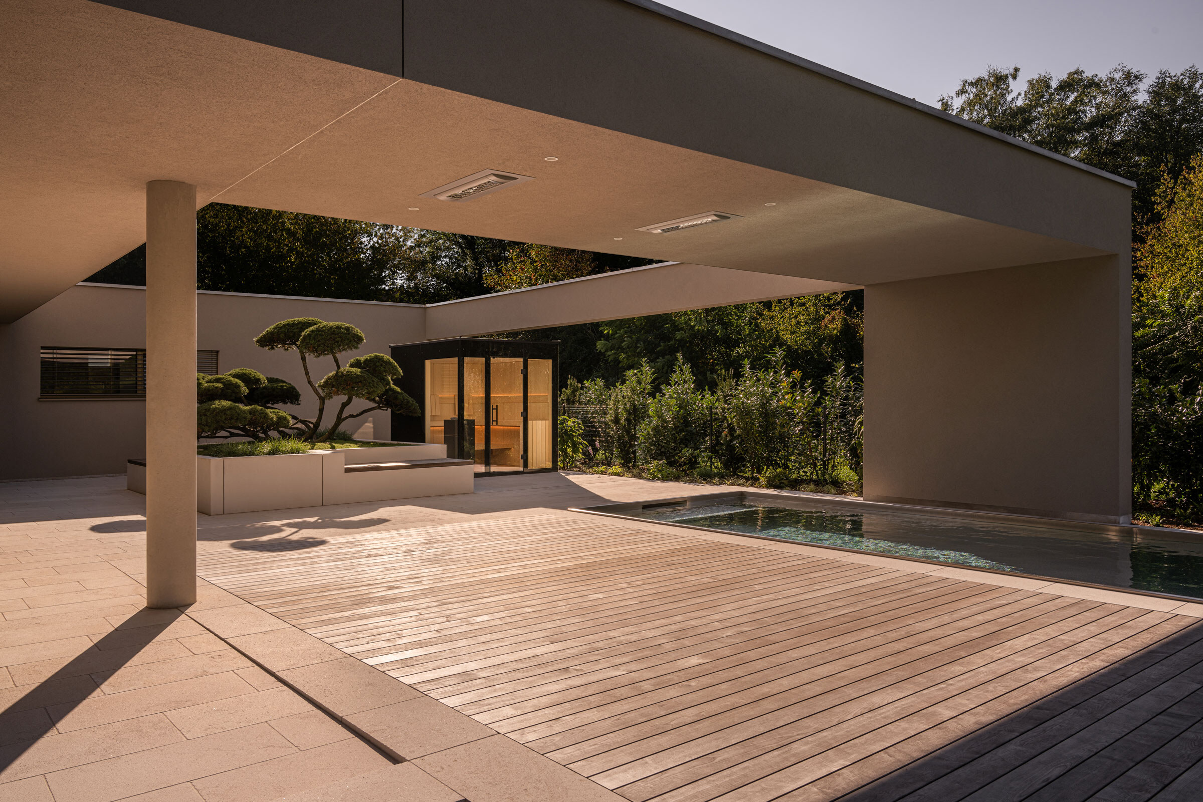 Moderne Außensauna mit schwarzer Verglasung auf einer Terrasse mit Pool und Gartenbonsai