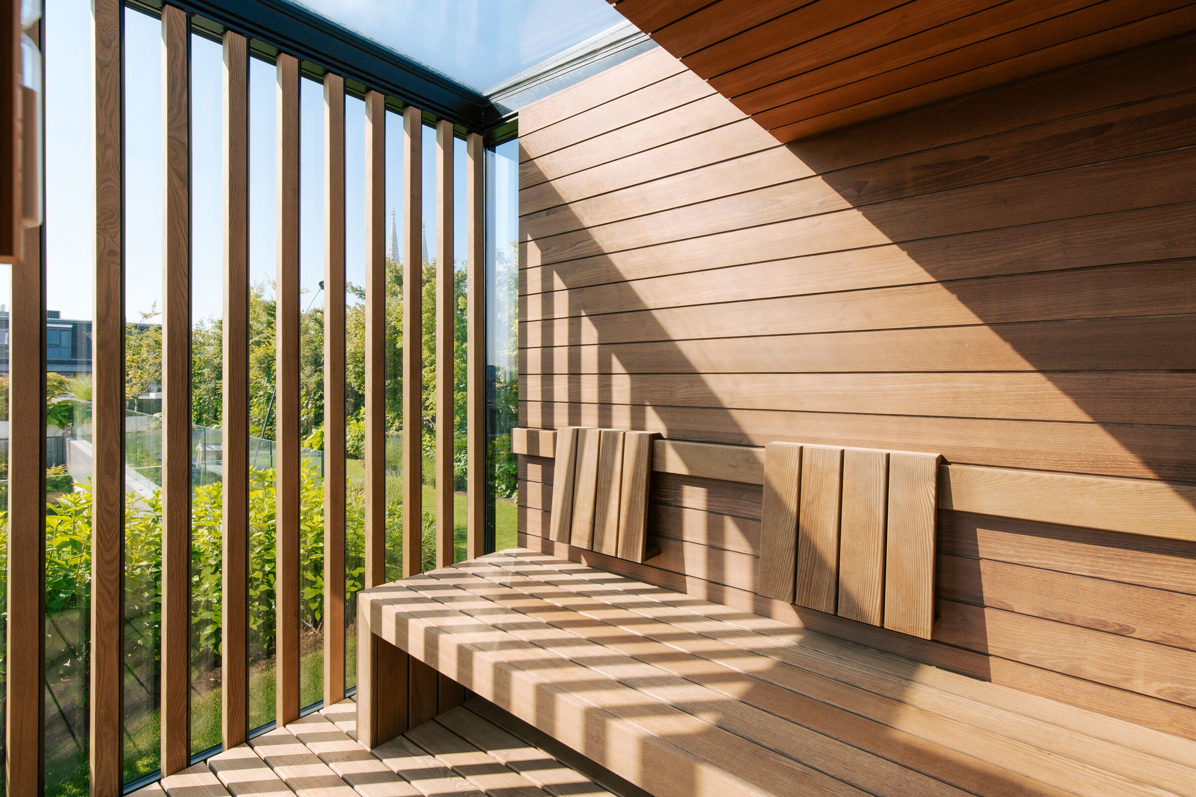 Moderne Sauna aus Akazienholz mit Verglasung, Sichtschutz aus Holzstreben und Ausblick in einen Dachgarten