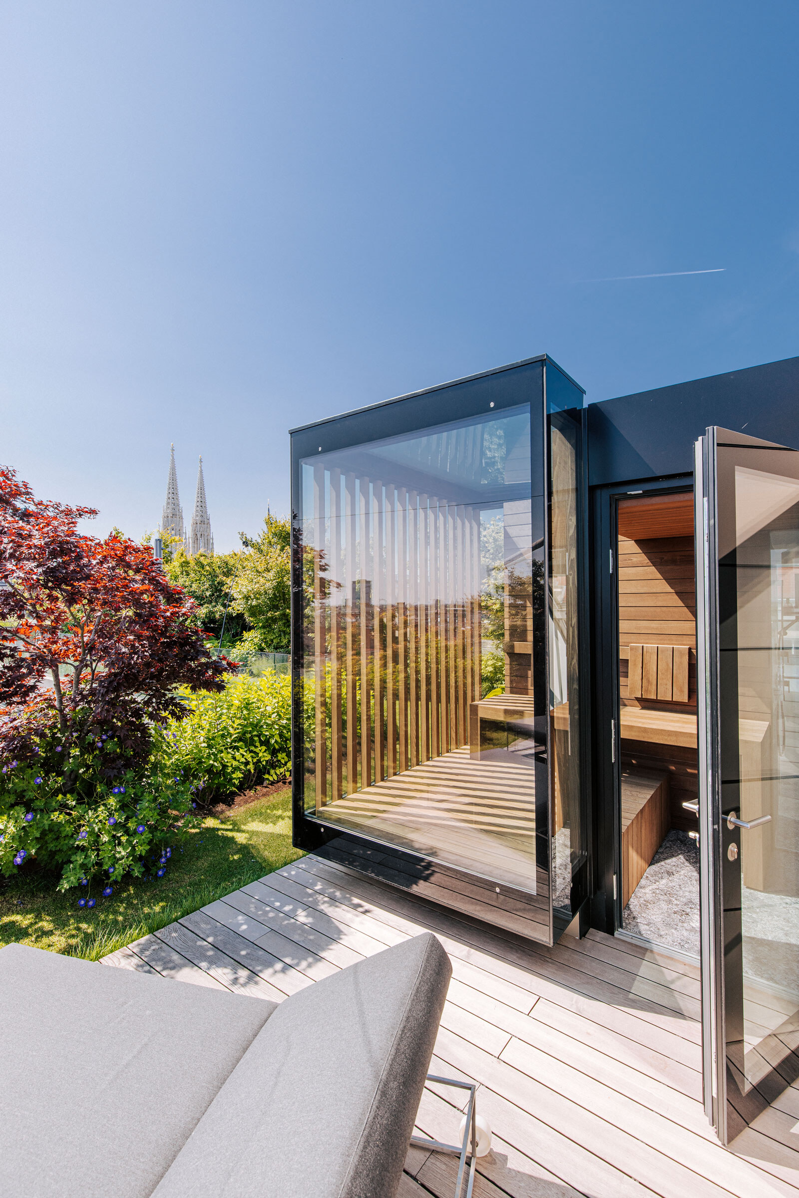 Individuelle, voll verglaste Outdoor-Sauna in modernem Design auf einer begrünten Dachterrasse vom Saunahersteller Deisl