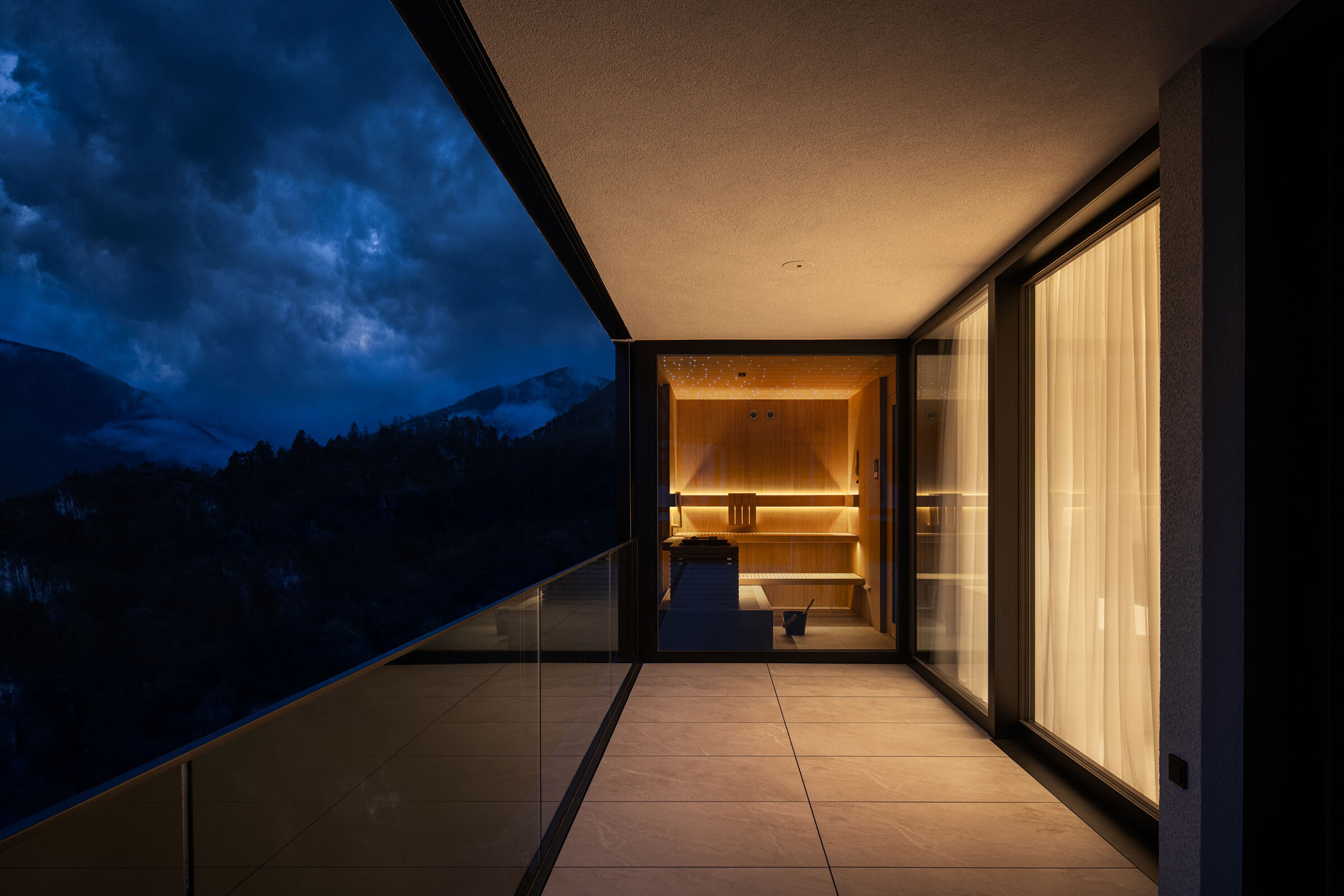 Moderne Sauna mit integriertem Sternenhimmel und Frontverglasung, sanft beleuchtet am Balkon in der Abendstimmung