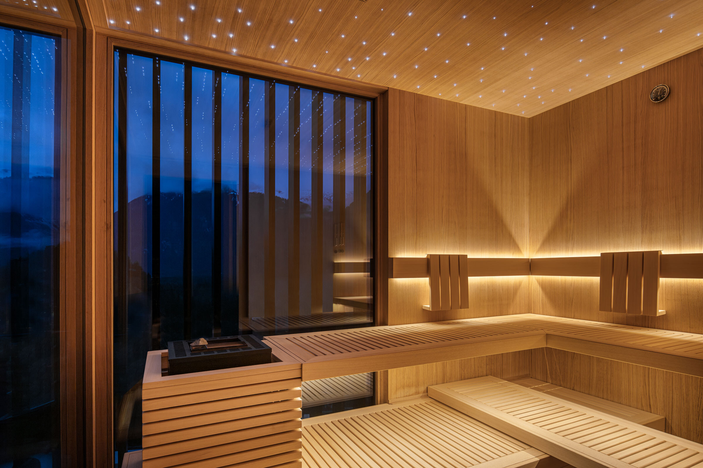 Moderne Sauna in individuellem Design aus hellem Holz, dezent beleuchtet mit integriertem Sternenhimmel in der Abenddämmerung