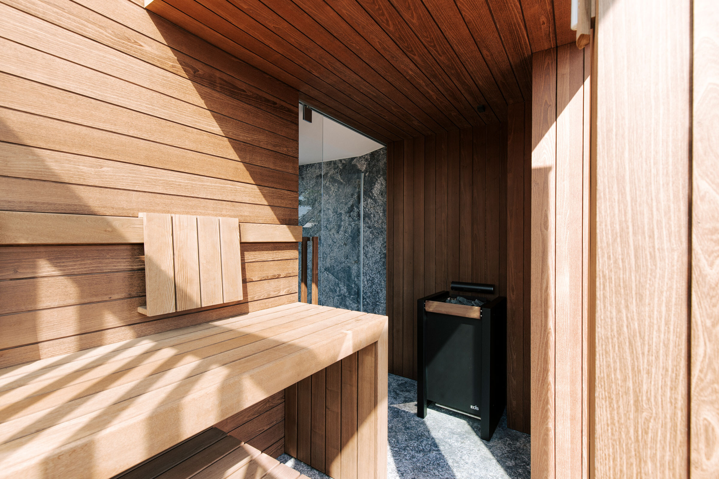 Maßgeschneiderte Sauna in modernem Design aus Thermoakazie mit Steinboden und Glastüre