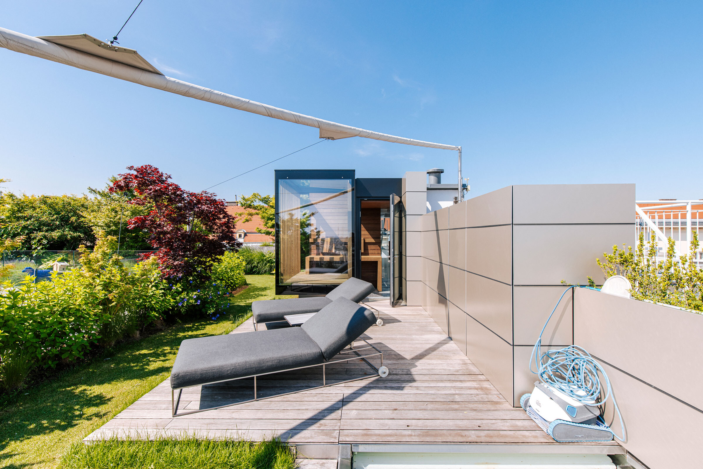 Vollverglaste Outdoor-Sauna in minimalistischem Design auf einer begrünten, modernen Dachterrasse