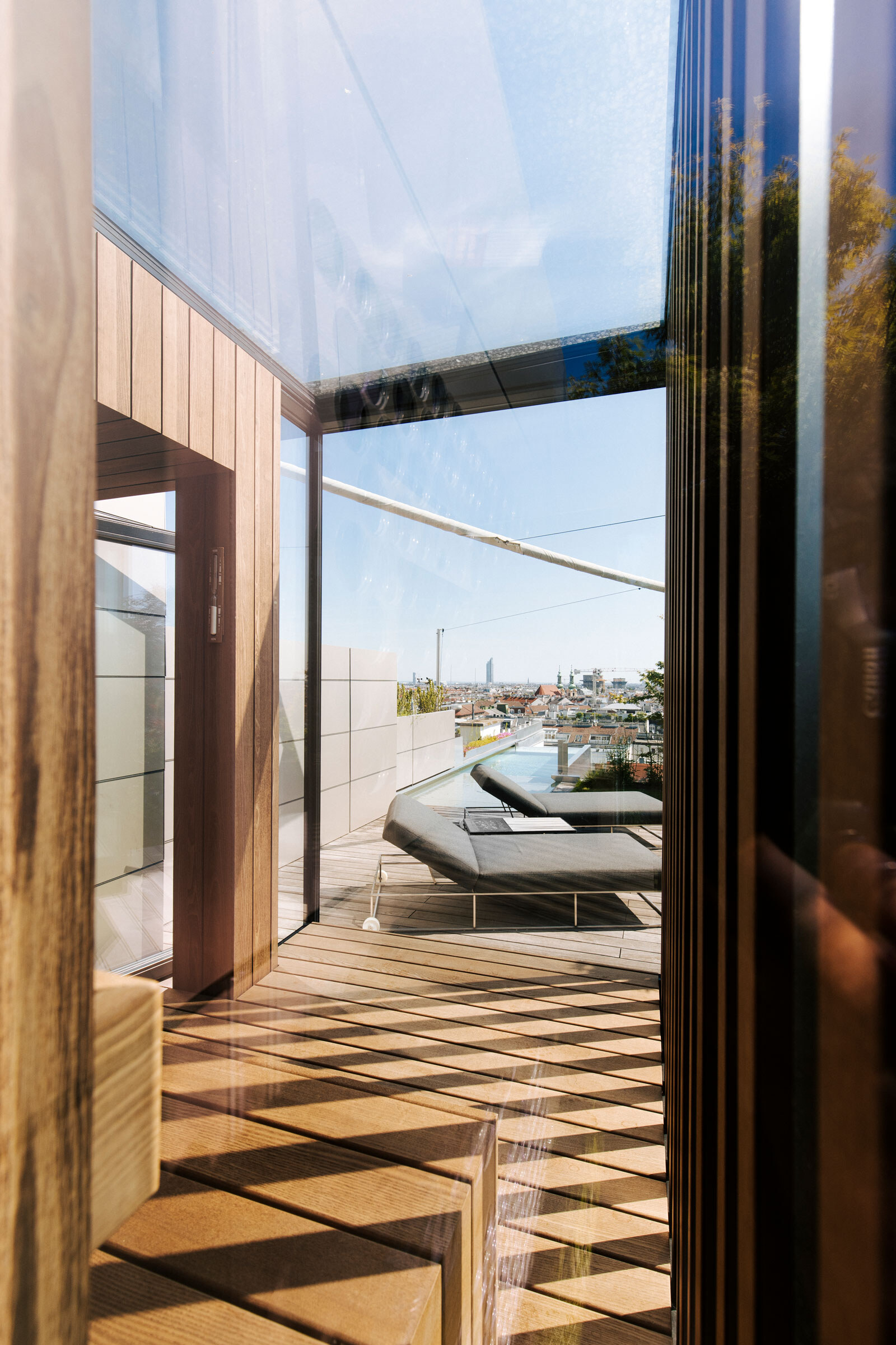 Verglaste Sauna nach Maß mit Ausblick auf eine moderne Dachterrasse mit Infinity-Pool