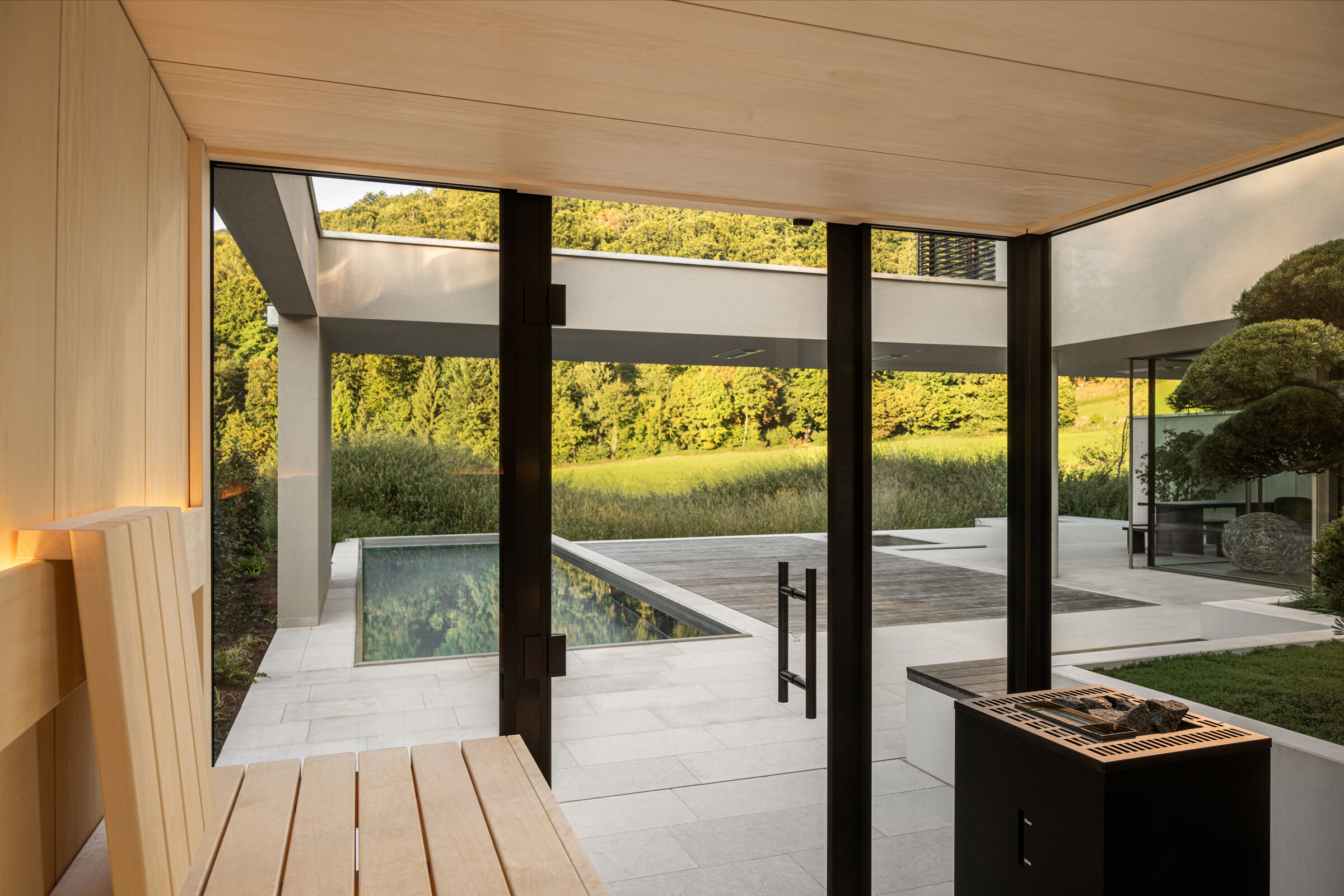 Ausblick aus einer verglasten Sauna auf eine moderne Terrasse mit Pool und großem Garten